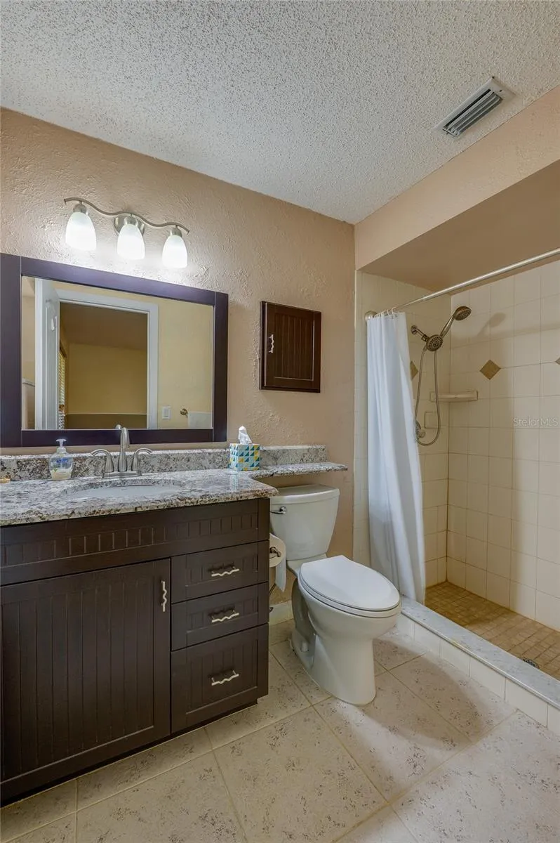 Primary bathroom showcasing a dark wood vanity with granite countertops, tiled flooring, a wide framed mirror, and a walk-in tiled shower.