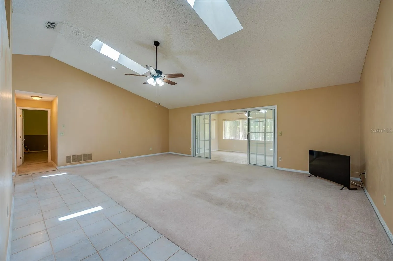 Expansive living room area featuring vaulted ceilings with skylights, carpeted flooring, and sliding glass doors that open to a sun room.