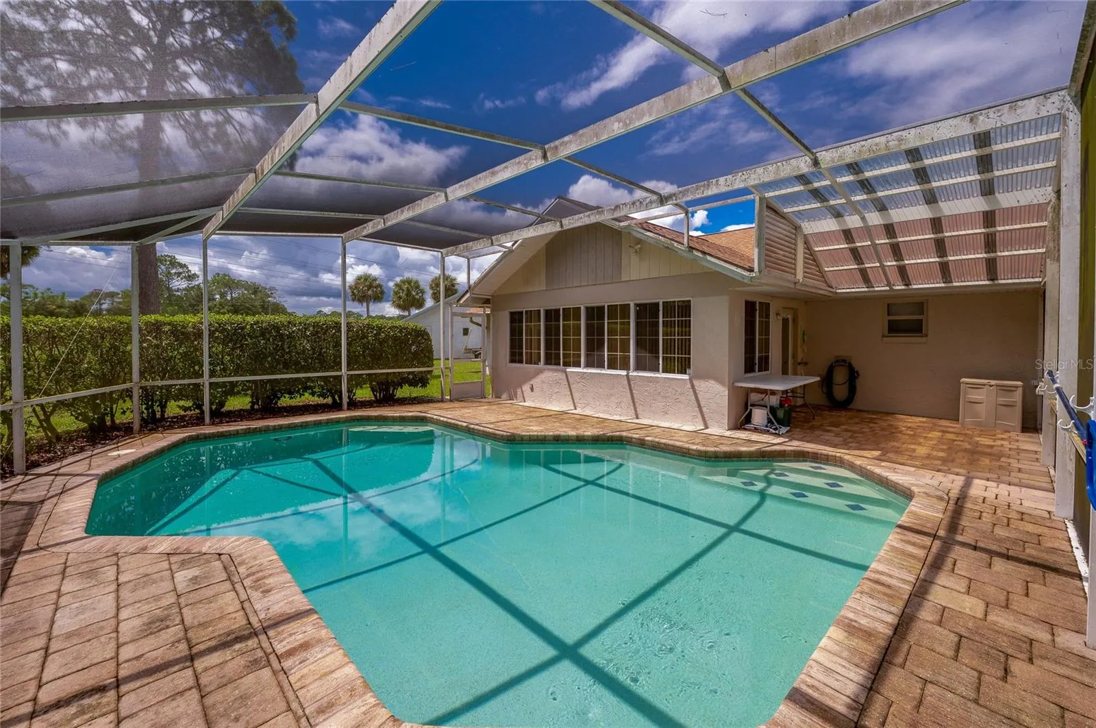 Spacious screened lanai showcasing an in-ground swimming pool, brick pavers, and direct access to the home.