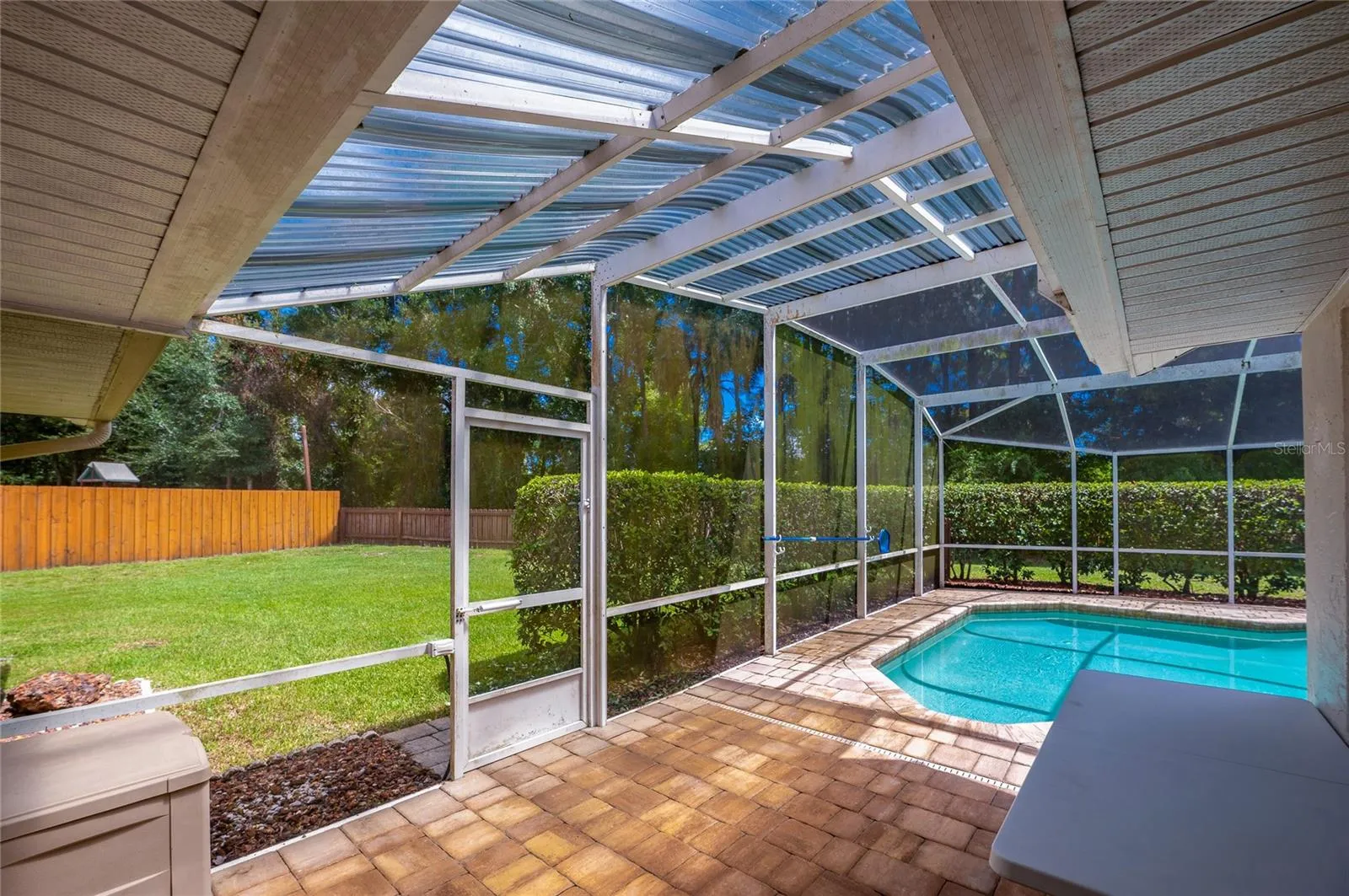 Paved patio area leading to a screened-in swimming pool enclosure with views of the grassy lawn.