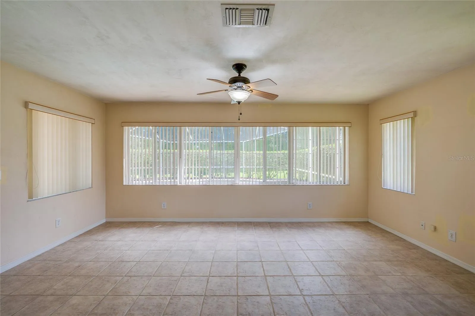 Bright enclosed sunroom equipped with light beige tile flooring, a ceiling fan, and wide windows fitted with vertical blinds for controlled light.
