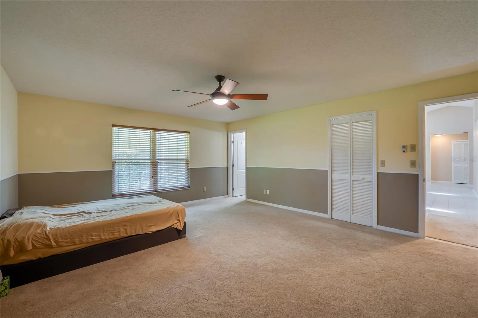 Generously sized bedroom offering wall-to-wall carpeting, two-tone neutral walls, a ceiling fan light fixture, and louvered closet doors.