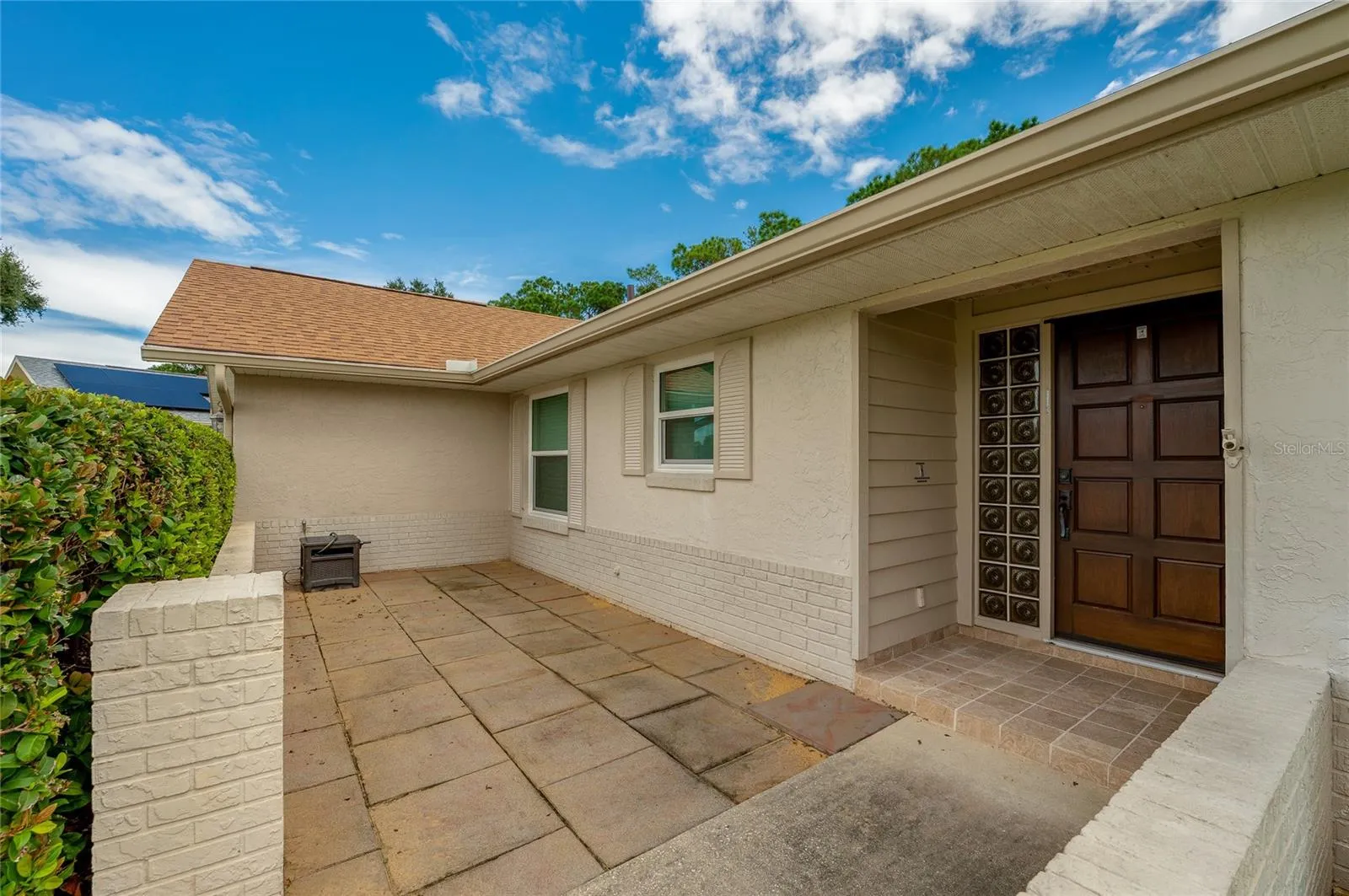 Welcoming front entry patio framed by brick half-walls, tiled walkways, and decorative glass block accents by the door.