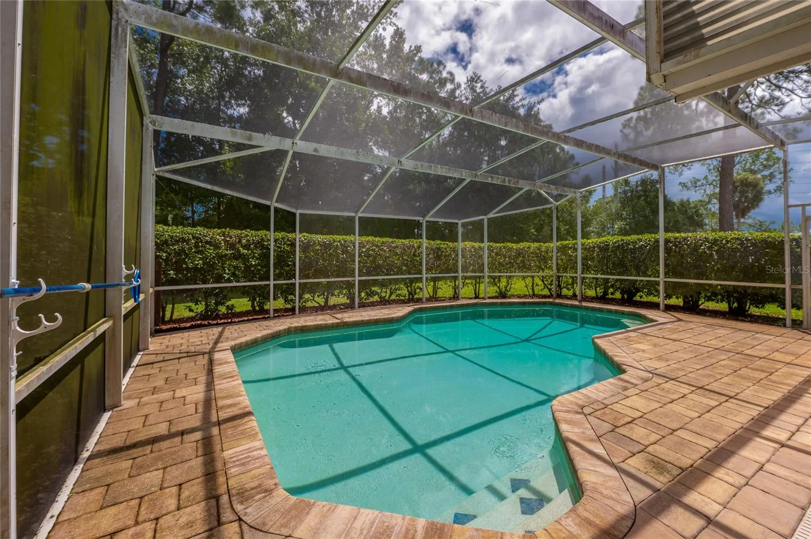 Screened-in pool deck area featuring a paved surround and private hedge line along the perimeter.