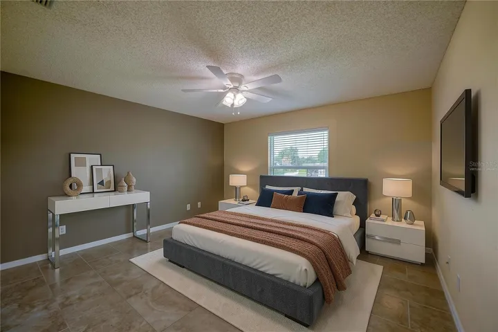 Virtually Staged - Generous bedroom featuring neutral tiled flooring, dual-tone walls, and a central ceiling fan with integrated lighting. Large window with blinds allows for ample natural light.
