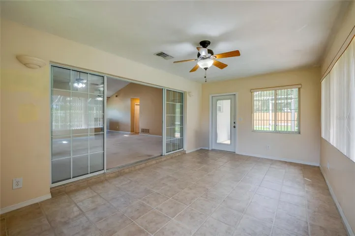 Versatile sunroom space featuring sliding glass entry doors, tile flooring, a ceiling fan fixture, and a exterior door providing outdoor access.