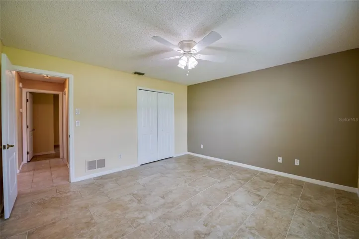 Spacious room showcasing easy-to-clean tile flooring, double closet doors, and an open doorway leading to adjacent hall spaces.