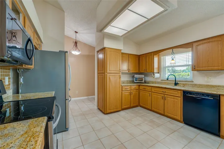 Well-appointed kitchen featuring solid wood cabinets, granite countertops, black and stainless steel appliances, and tile flooring.