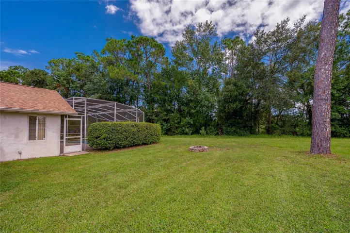 Expansive grassy backyard featuring a stone fire pit, mature trees, and a view of the pool enclosure.