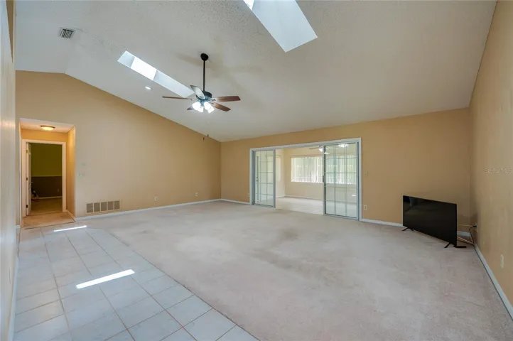 Expansive living room area featuring vaulted ceilings with skylights, carpeted flooring, and sliding glass doors that open to a sun room.