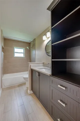 Full bathroom with modern tile flooring, custom dark cabinetry, and open storage. A tiled tub-and-shower combo and elegant wall lighting complete the space.