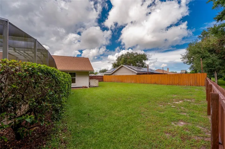 Fenced side yard with a generous stretch of green lawn and mature hedging along the pool structure.