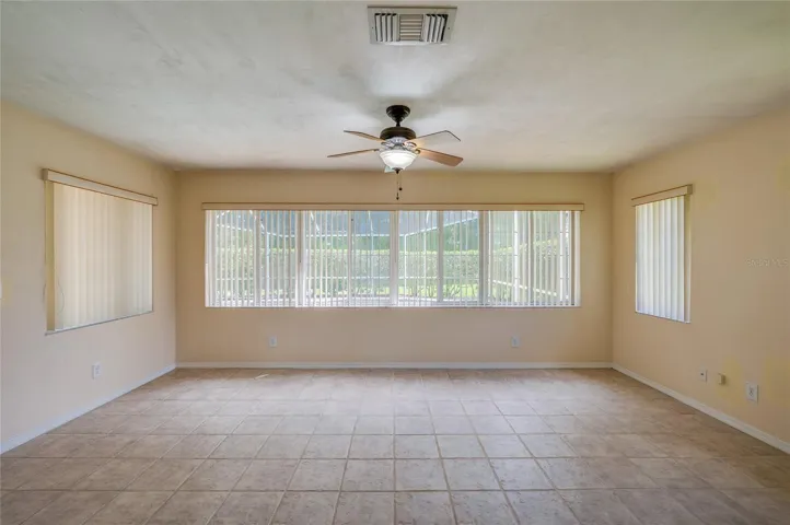 Bright enclosed sunroom equipped with light beige tile flooring, a ceiling fan, and wide windows fitted with vertical blinds for controlled light.