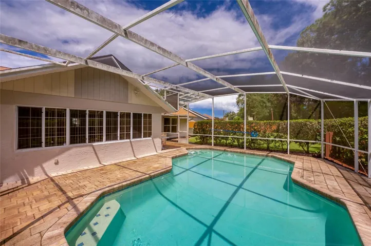 Alternate angle of the screened swimming pool enclosure, highlighting the extensive paved deck and home exterior.