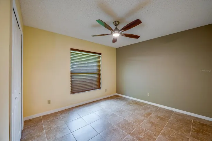 Cozy bedroom offering neutral tile floors, warm wall tones, a modern ceiling fan, and built-in closet space. Window blinds provide light control and privacy.