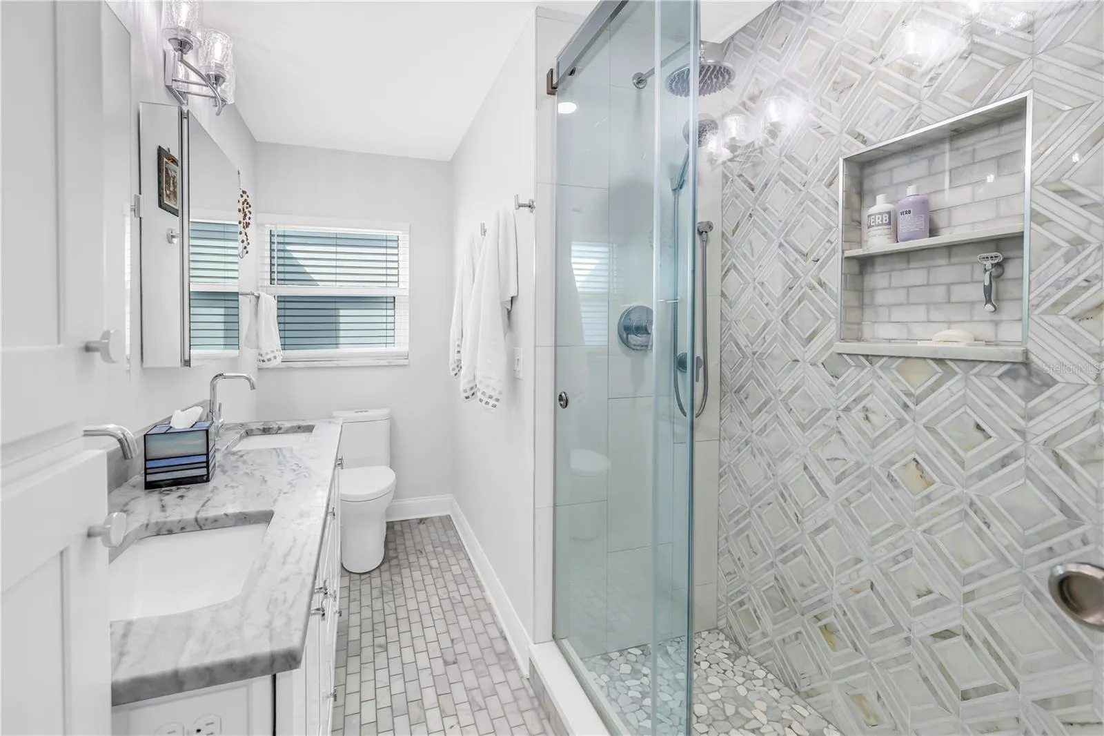 Primary bath with designer shower with spa stones and Art Deco influenced sand and sea aesthetic and built- in shower niche.