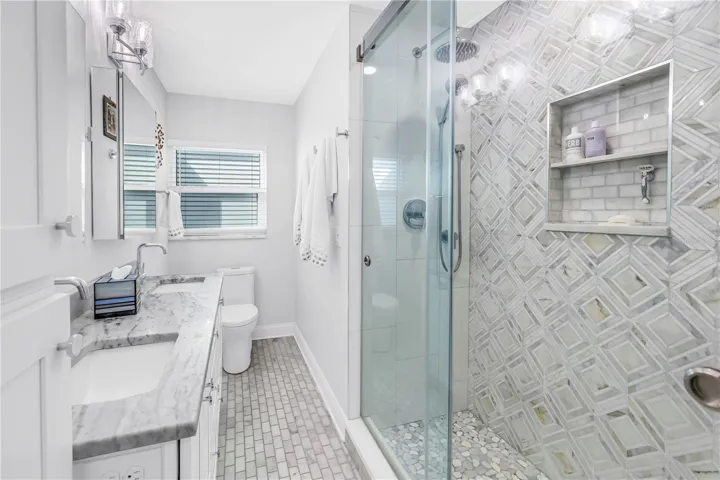 Primary bath with designer shower with spa stones and Art Deco influenced sand and sea aesthetic and built- in shower niche.