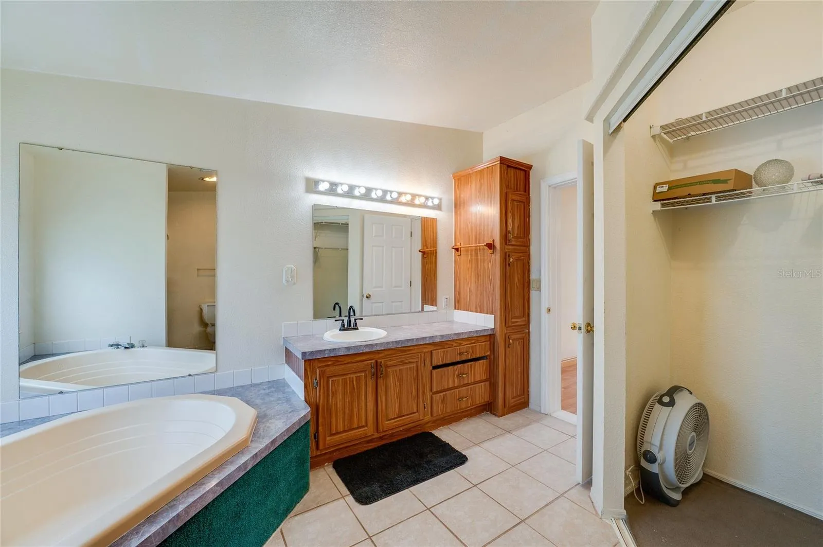 Additional view of the primary bath highlights the corner soaking tub, extended vanity, generous cabinetry, large mirrors, and adjacent closet storage.