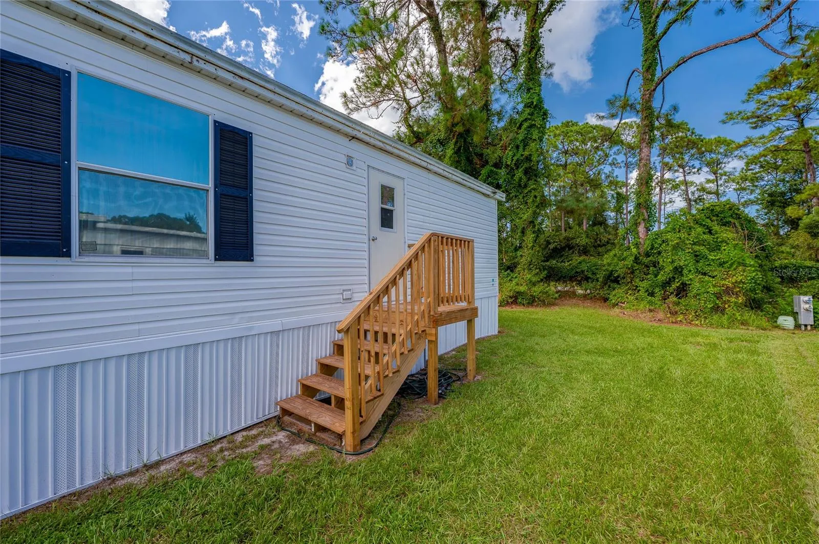 Rear entry features wood steps with railings leading to the home, opening directly to the surrounding lawn.