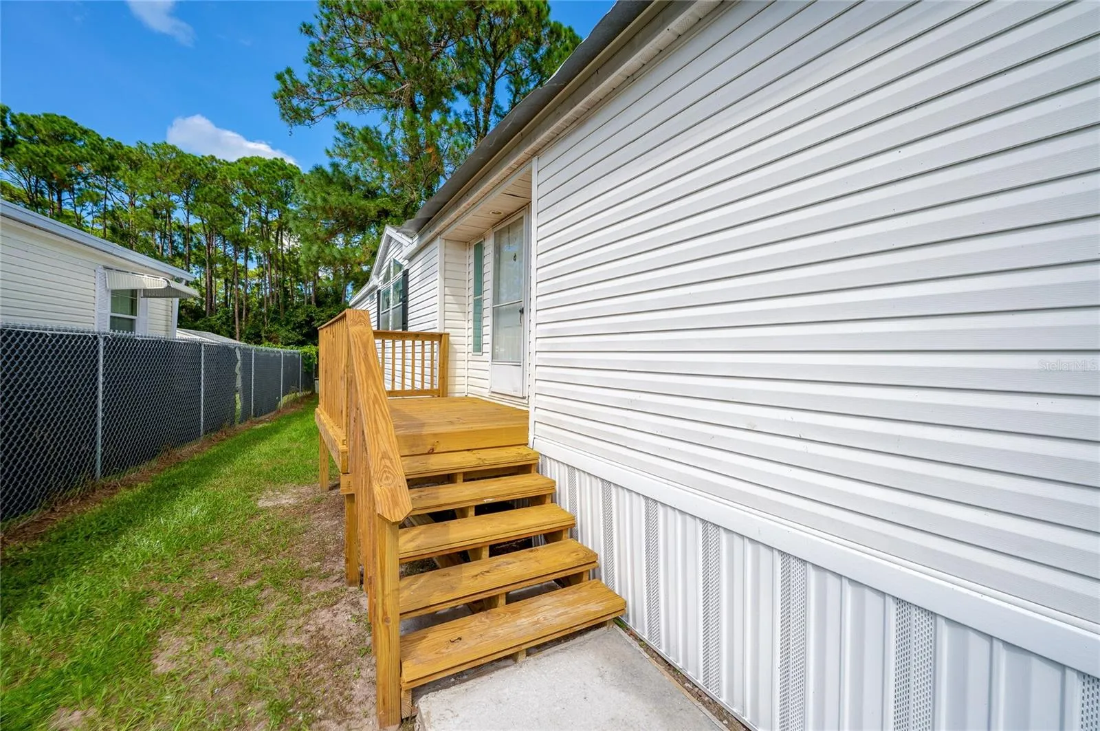Wood steps and a raised landing provide access to the home, with a grassy side yard alongside the residence.