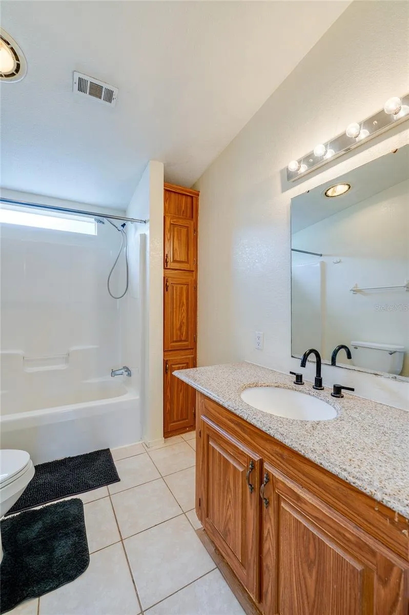 Full bathroom offers a tub-and-shower combination, vanity with generous counter space, large mirror, tile flooring, and additional built-in storage.