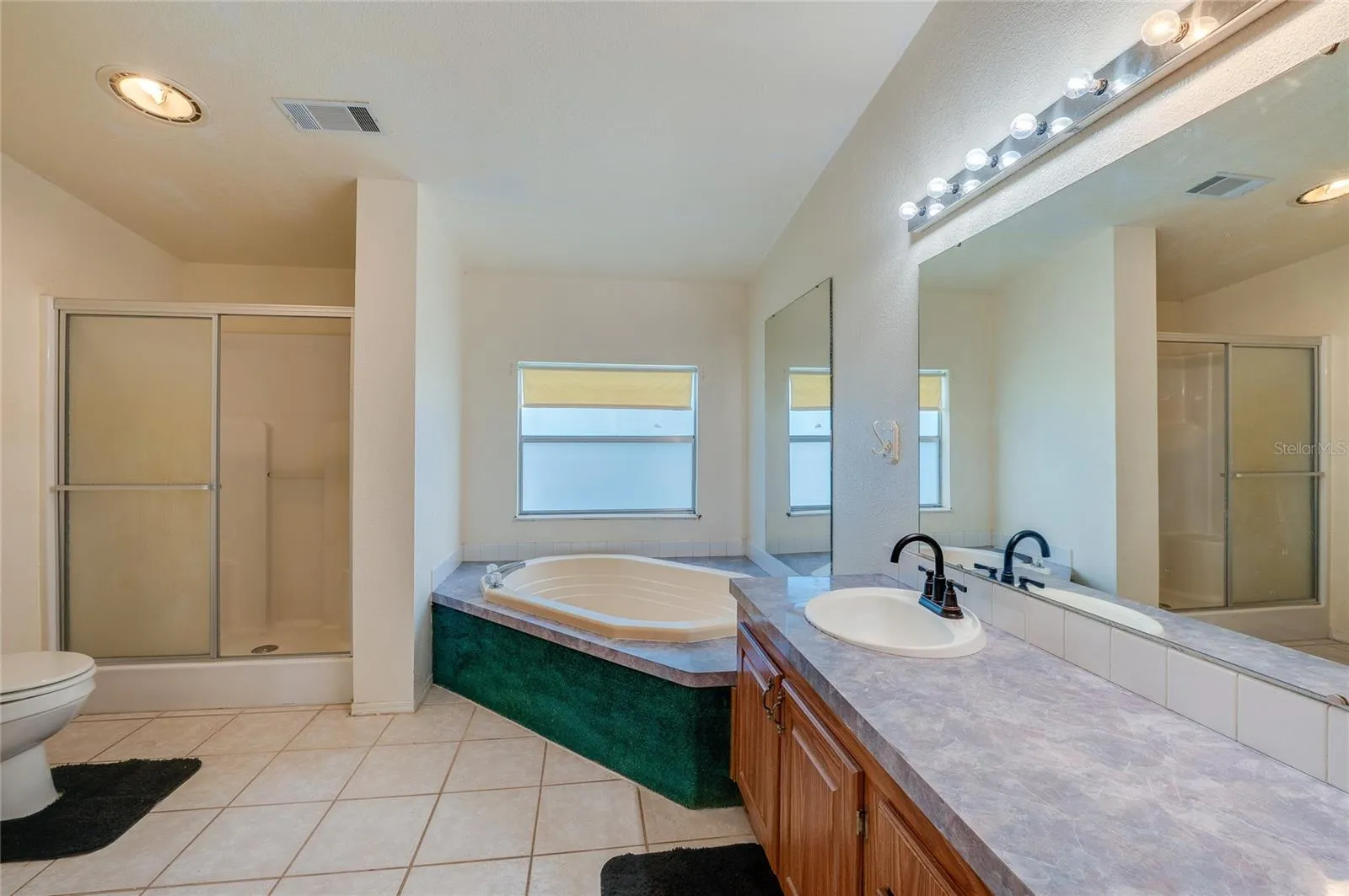 Large bathroom includes a corner soaking tub, separate enclosed shower, extended vanity with oversized mirror, and tile flooring.
