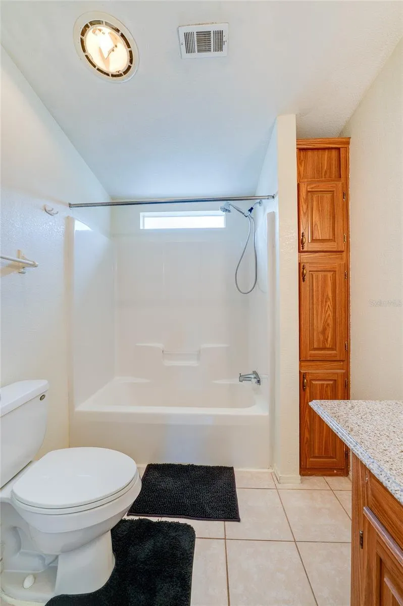 Additional view highlights the tub-and-shower combination, natural light from a high window, and tall built-in storage cabinetry.