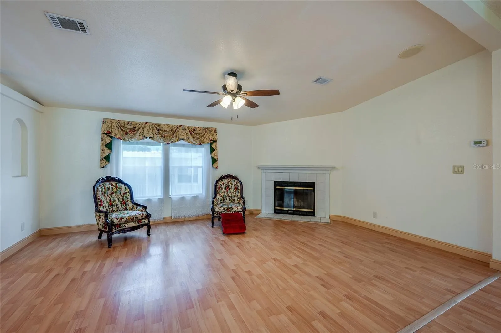 Bright living room offers plenty of flexibility for seating and entertaining, with a fireplace, ceiling fan, and large front-facing windows.