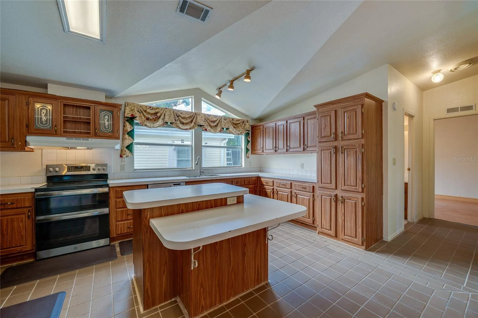Another angle showcases the kitchen's generous cabinet storage, center island with multiple work surfaces, large windows, and vaulted architectural detail overhead.