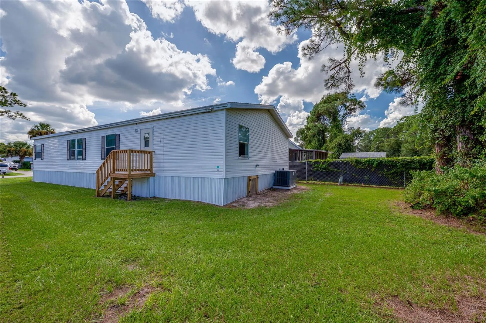 Wide exterior view showcases the home’s rear and side elevations, wood entry steps, open lawn, and mature greenery along the property perimeter.