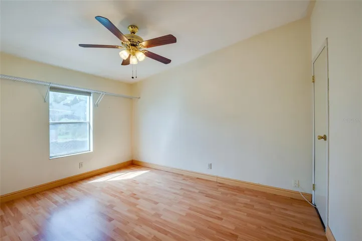 Bright bedroom features a ceiling fan, window for natural light, and ample open space for flexible furniture placement.