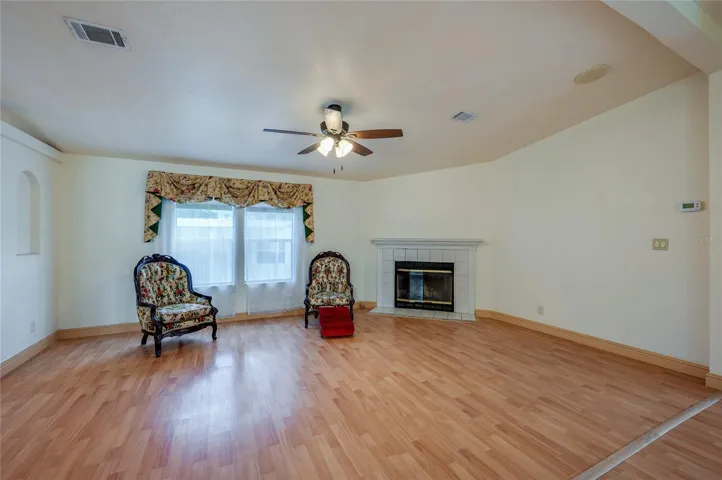 Bright living room offers plenty of flexibility for seating and entertaining, with a fireplace, ceiling fan, and large front-facing windows.