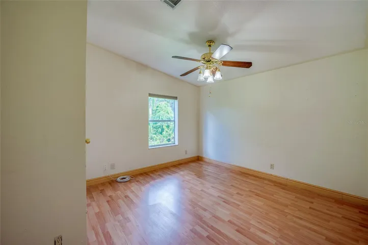 Spacious bedroom offers a ceiling fan, natural light from a large window, and ample wall space for flexible furniture placement.
