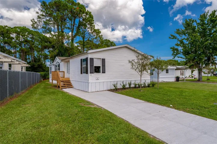Front approach features a concrete walkway leading to a raised entry with wood steps, complemented by an open lawn and established landscaping.
