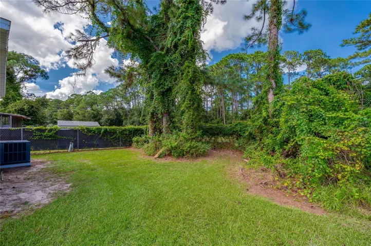 Open grassy yard is bordered by established trees and greenery, providing additional outdoor space behind the home.