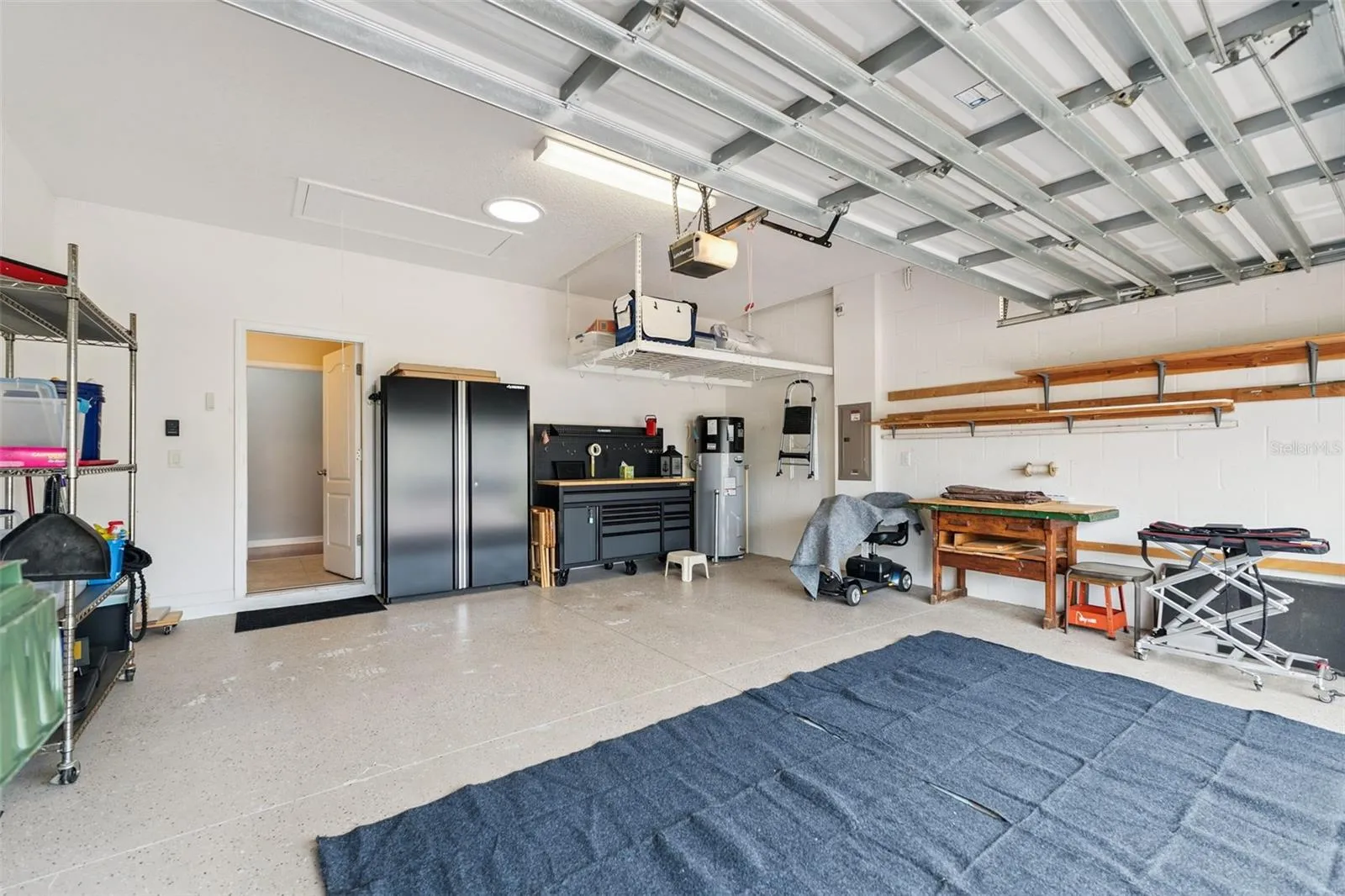 The garage equipped with 3 overhead storage racks, workbench with matching cabinetry, and an overhead solar skylight