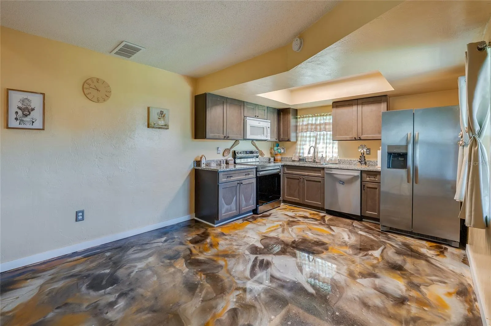 Functional kitchen equipped with stainless steel appliances, dark wooden cabinetry, granite countertops, and epoxy flooring.