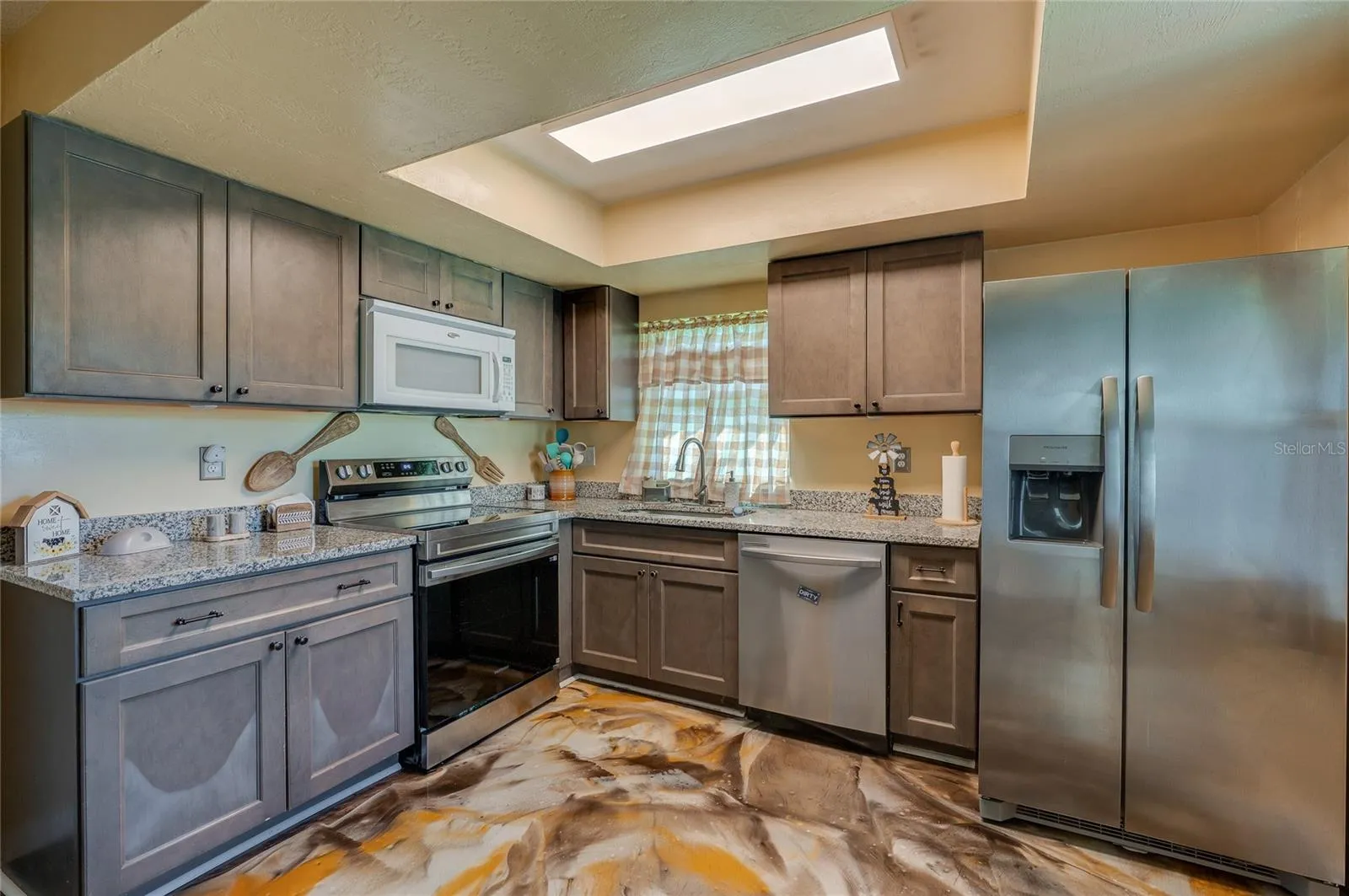 Upgraded kitchen area highlighting a full suite of stainless steel appliances, recessed ceiling light box, and custom epoxy flooring.