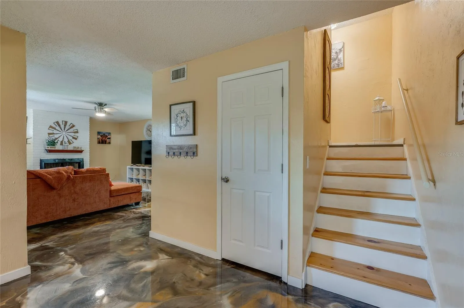 Foyer and entryway showing wooden stair steps with white risers, epoxy flooring, and access to an adjacent living area.