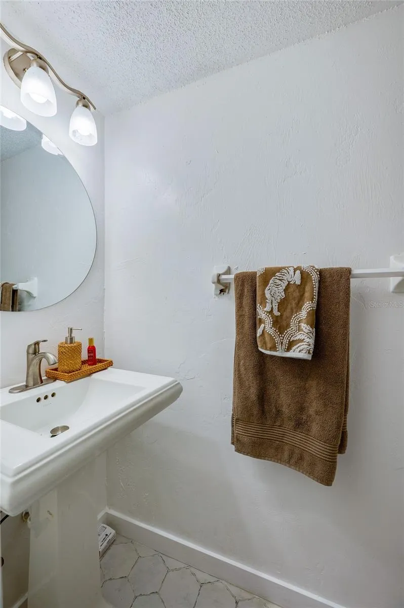 Compact half-bathroom with a white pedestal sink, rounded wall mirror, and modern lighting fixture.