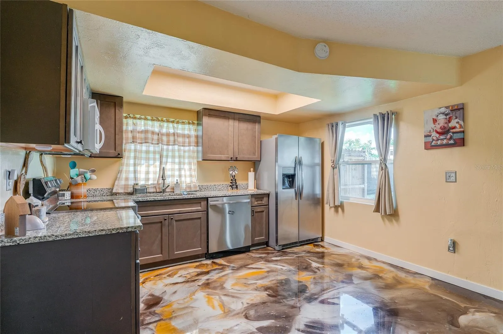 Functional kitchen space featuring stainless steel appliances, dark cabinetry, granite countertops, and eye-catching epoxy flooring.