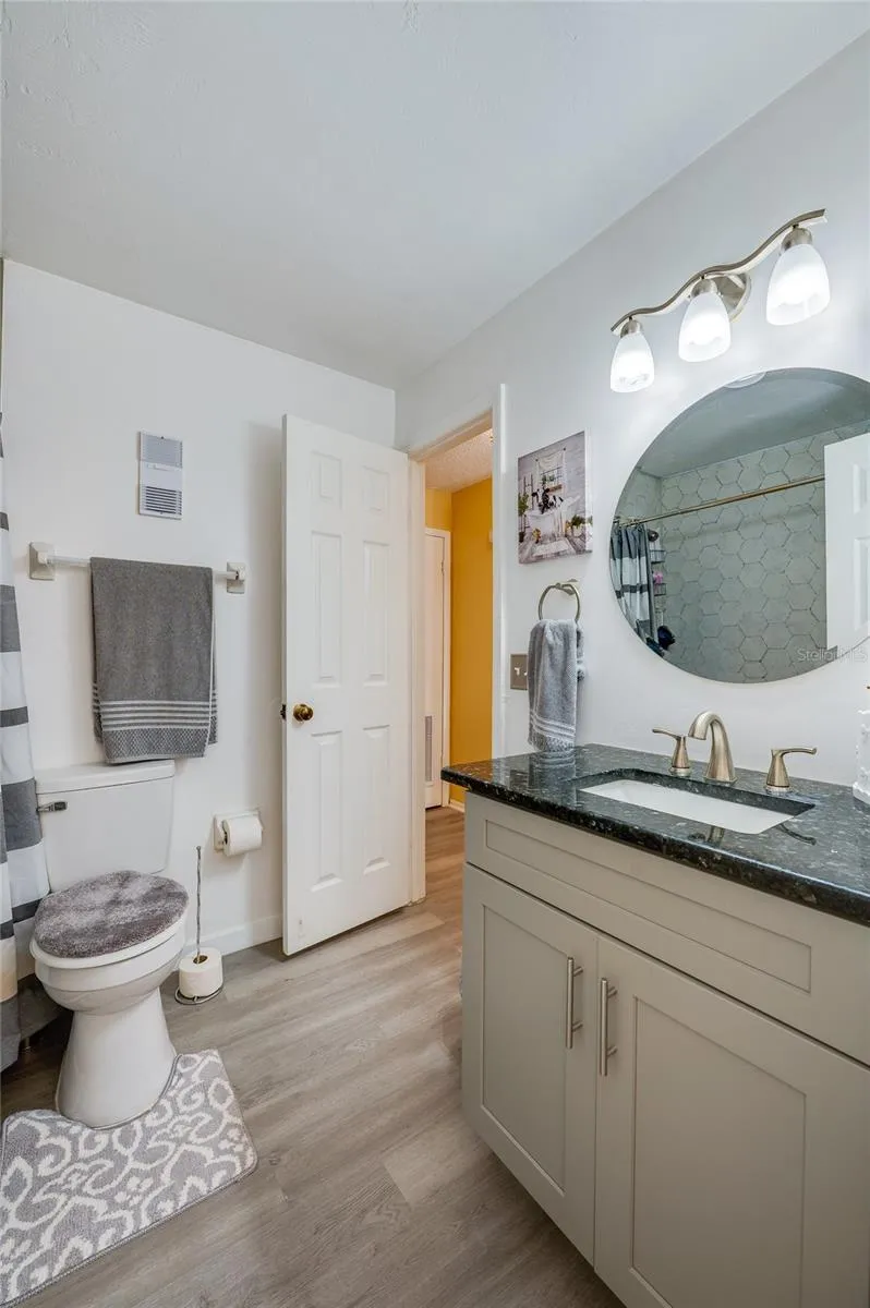 Full bathroom featuring a vanity with dark granite countertops, LVP flooring, and a circular wall mirror.