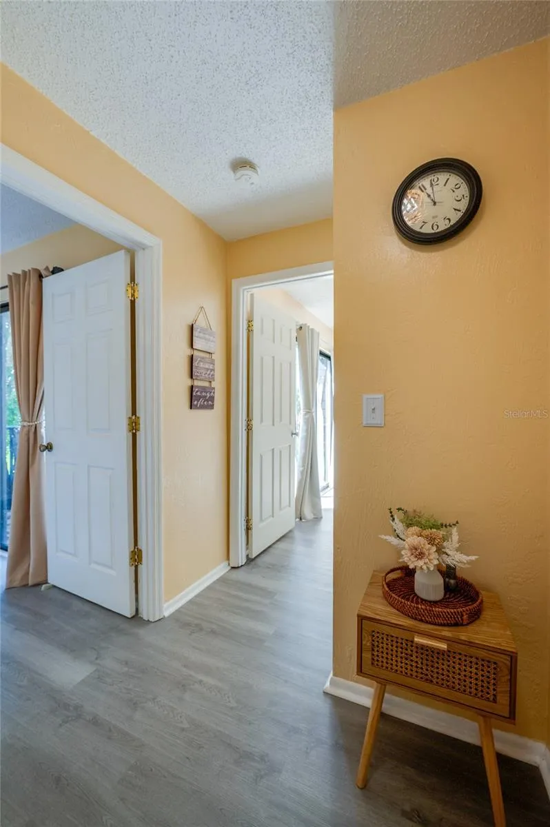 Bright, welcoming hallway featuring light wood-look flooring, warm yellow walls, and smooth transitions to adjacent rooms.