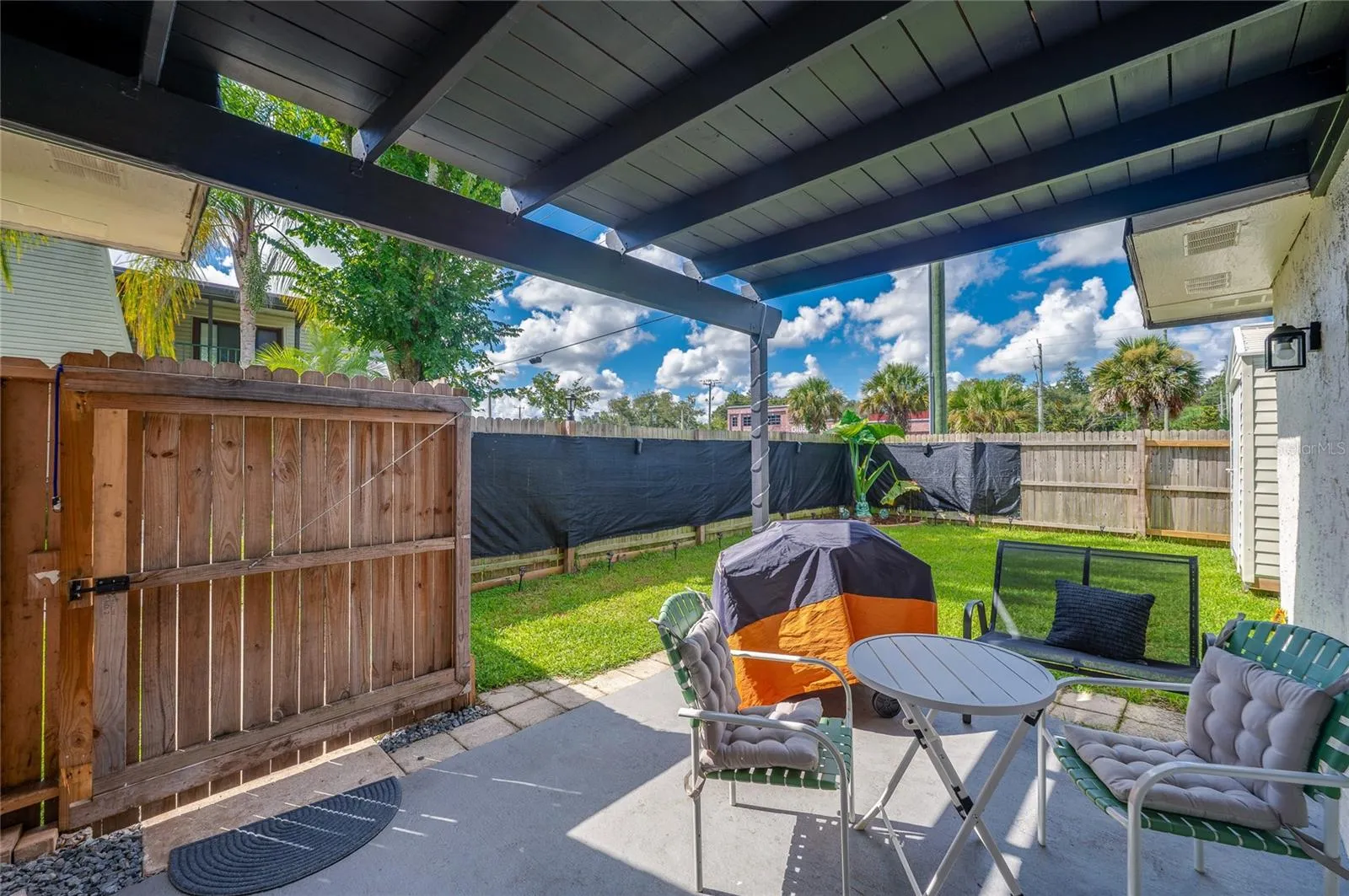 Covered ground-floor patio leading out to a fully fenced private yard framed by lush green grass.