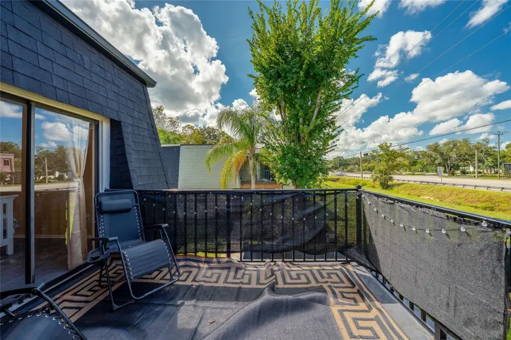 Private upper-level balcony featuring black mesh privacy screening, a patterned floor mat, and open views of surrounding green space.