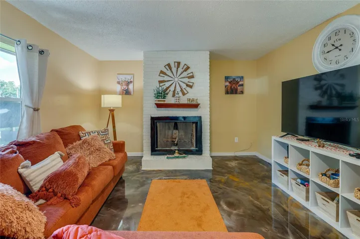 Cozy living room space centered around a painted white brick fireplace and hearth with large windows allowing for ample natural light.