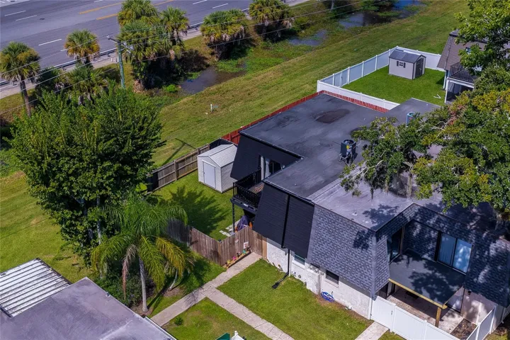 Aerial view of a residential property surrounded by lush greenery, featuring fenced yard space, storage shed, and a balcony.