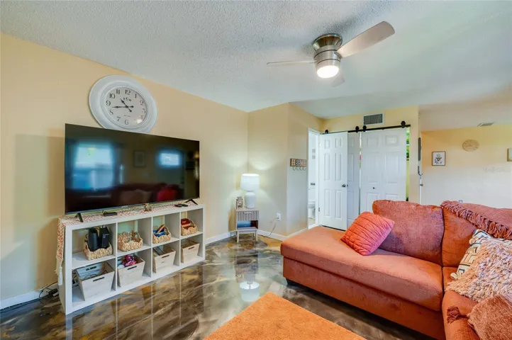 Inviting living space highlights striking epoxy floor finishes, a ceiling fan, and white sliding barn doors for a modern touch.