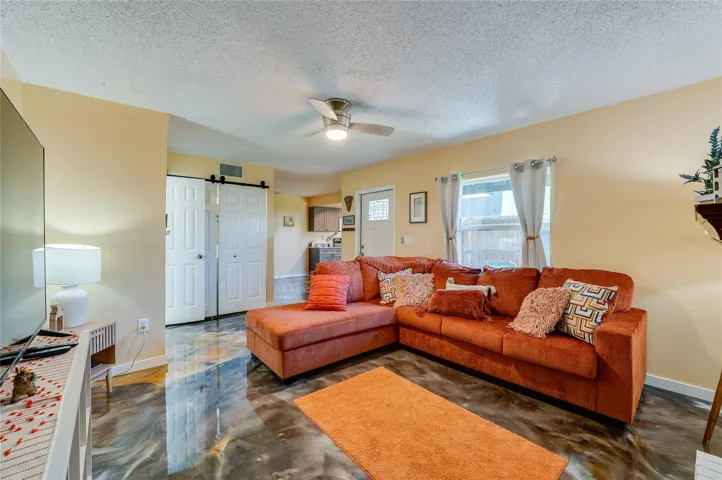Bright living area featuring epoxy floors, a white front entrance door, and sliding closet doors leading to adjoining spaces.
