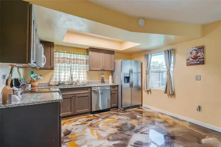 Functional kitchen space featuring stainless steel appliances, dark cabinetry, granite countertops, and eye-catching epoxy flooring.